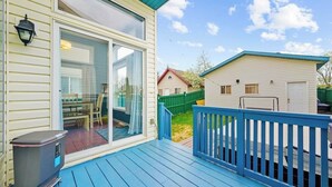 A house with a blue deck, a sliding glass door, and a small shed in the backyard.