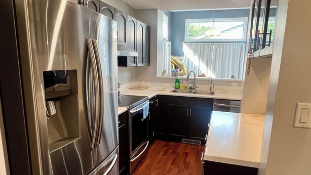 A modern kitchen with stainless steel appliances, dark cabinetry, and a wooden floor.