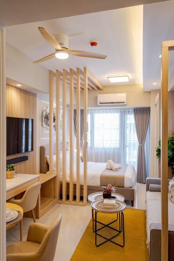 A modern hotel room with a bed, a desk, a TV, a ceiling fan, and an air conditioning unit.