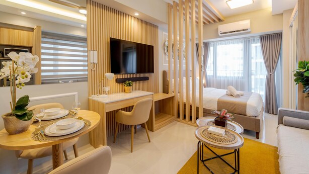 A modern hotel room with a wooden desk, a bed, a sofa, and a TV. - Sleek and Stylish 1br in Mall Of Asia Complex (Pasay)