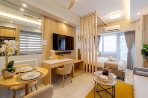 A modern hotel room with a wooden desk, a bed, a sofa, and a TV.