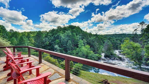 Terraza con sillas Adirondack rojas que da a un río y un bosque.