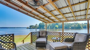 Une terrasse couverte, dotée de meubles en osier, d’un ventilateur et offrant une vue sur un lac et une forêt.