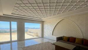 A spacious room with a high ceiling, a large window, and a sofa with cushions.