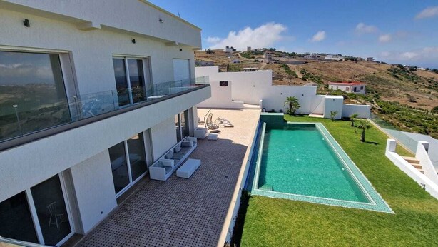 A modern house with a rooftop pool, a covered patio, and a view of the surrounding landscape.