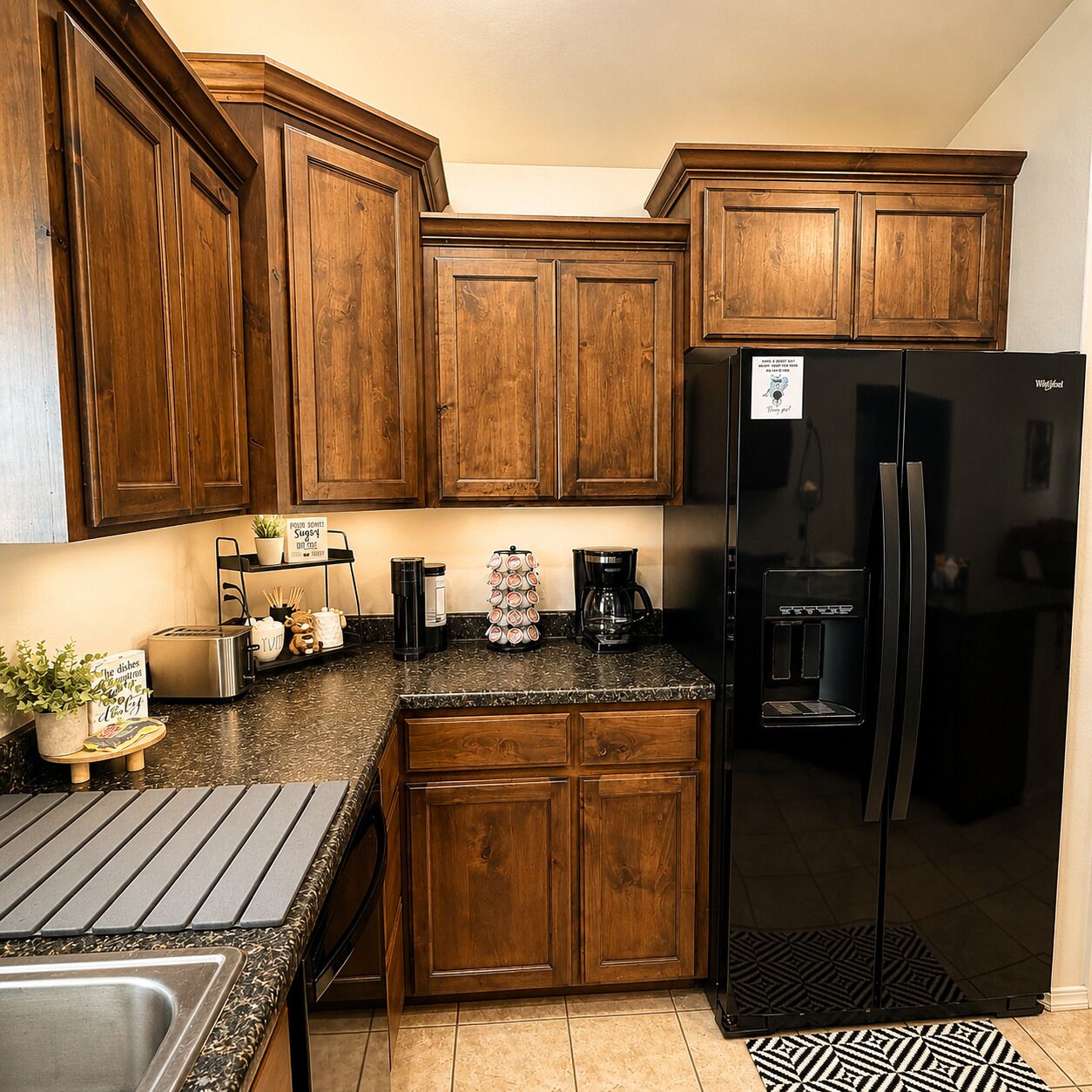 Una cocina con armarios de madera, un refrigerador negro, una cafetera y una pequeña planta.