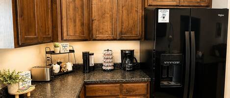 Una cocina con armarios de madera, un refrigerador negro, una cafetera y una pequeña planta.