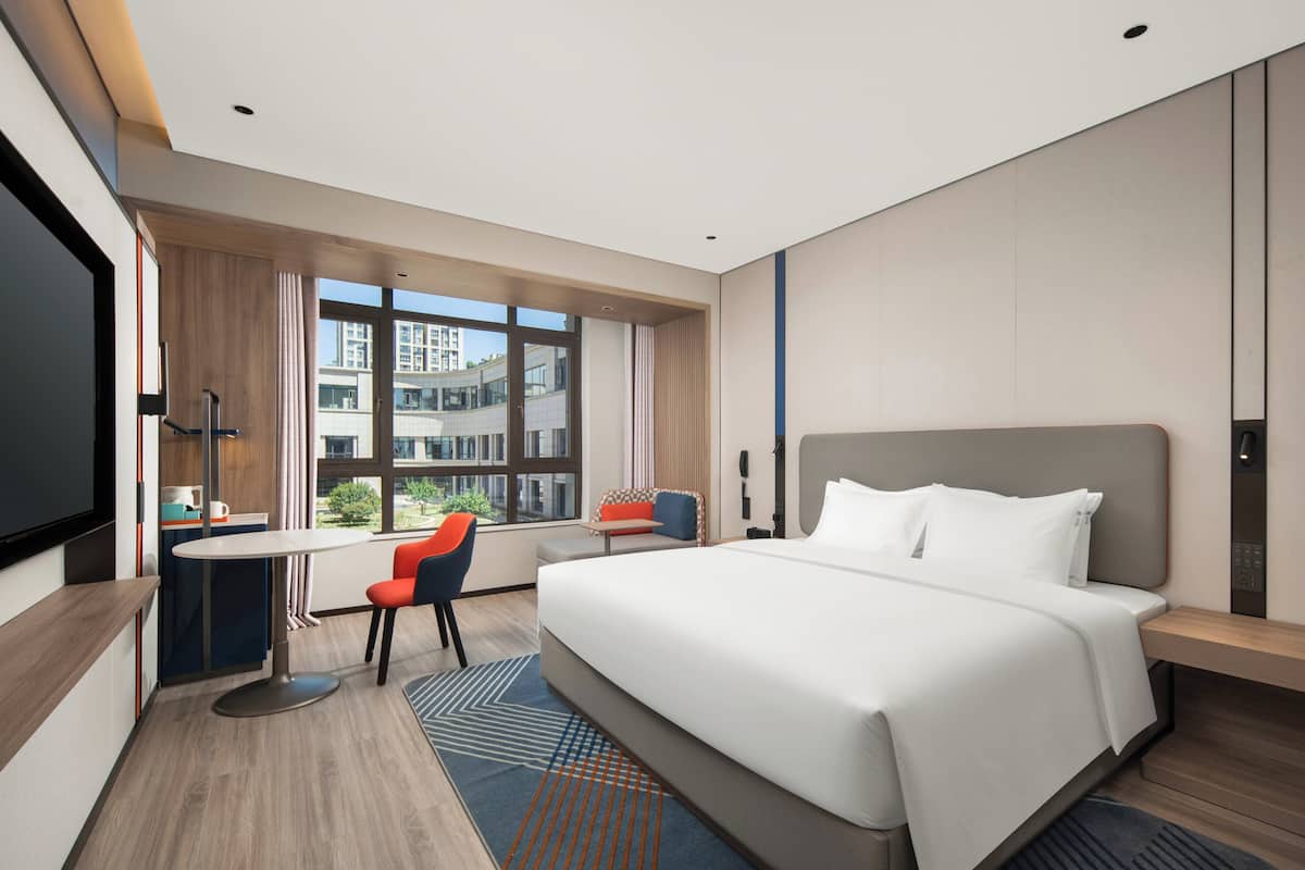 Una habitación de hotel moderna con una cama grande, un escritorio y una silla. Hay una ventana con vistas a edificios.