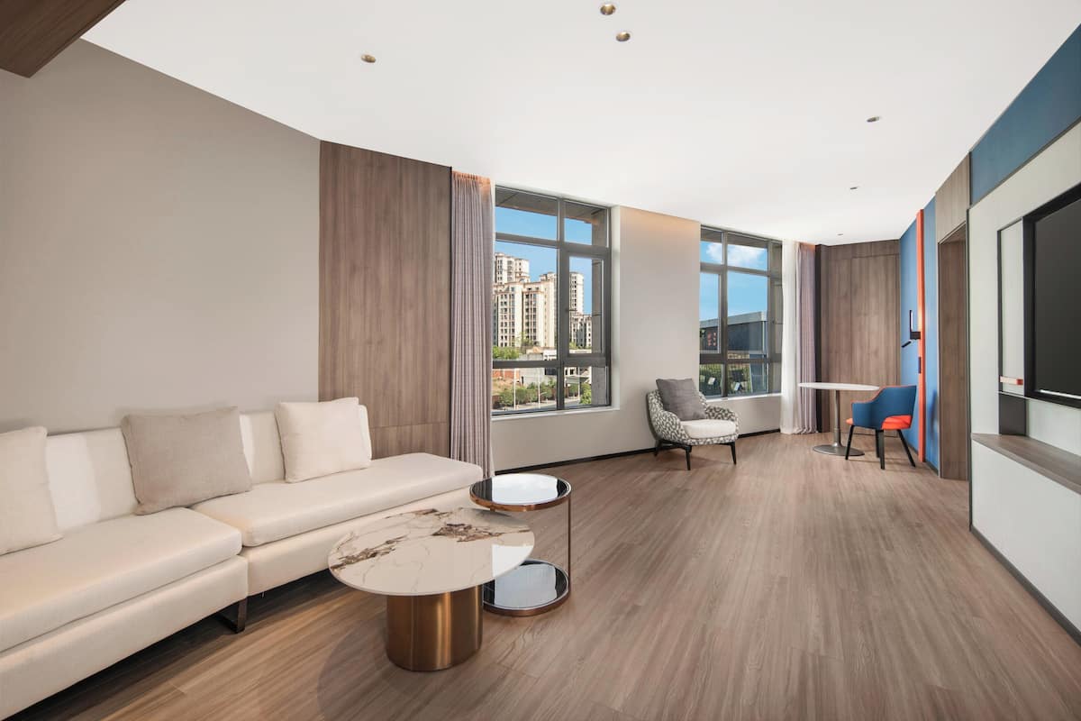 Una sala de estar moderna con un sofá, una mesa de centro y sillones, ventanas amplias con vista a la ciudad y un televisor de pantalla plana.