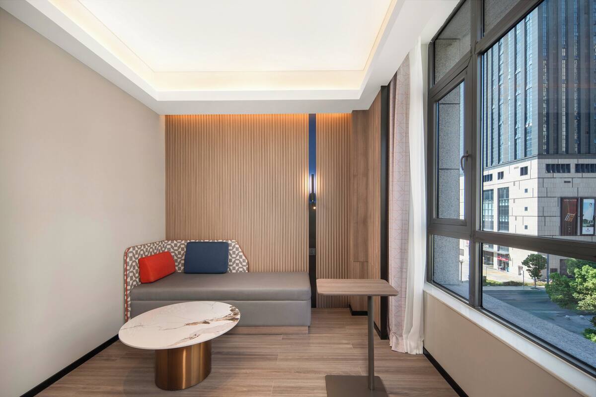 Una habitación moderna con sofá, una mesita y un ventanal grande con vistas a la ciudad.