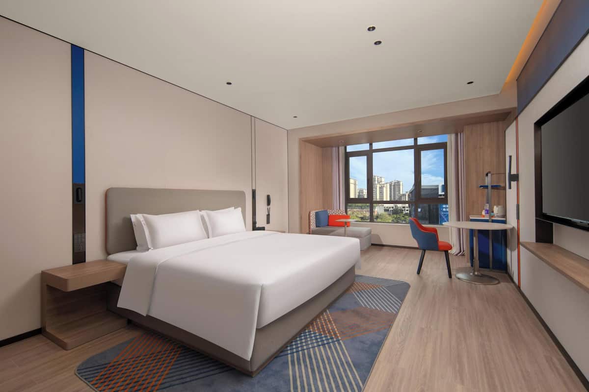 Una habitación de hotel moderna con una cama grande, un escritorio con silla, un televisor y una ventana con vista a la ciudad.