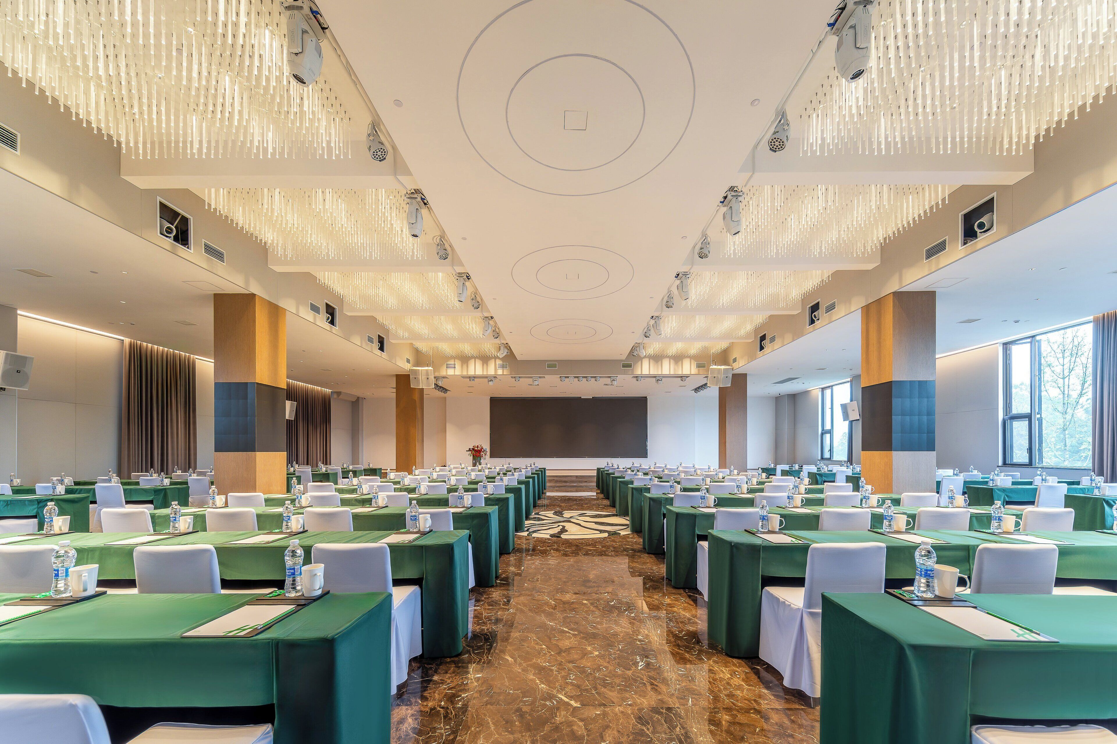 Un salón de conferencias con filas de mesas, una pantalla grande al frente y un moderno diseño de candelabro.