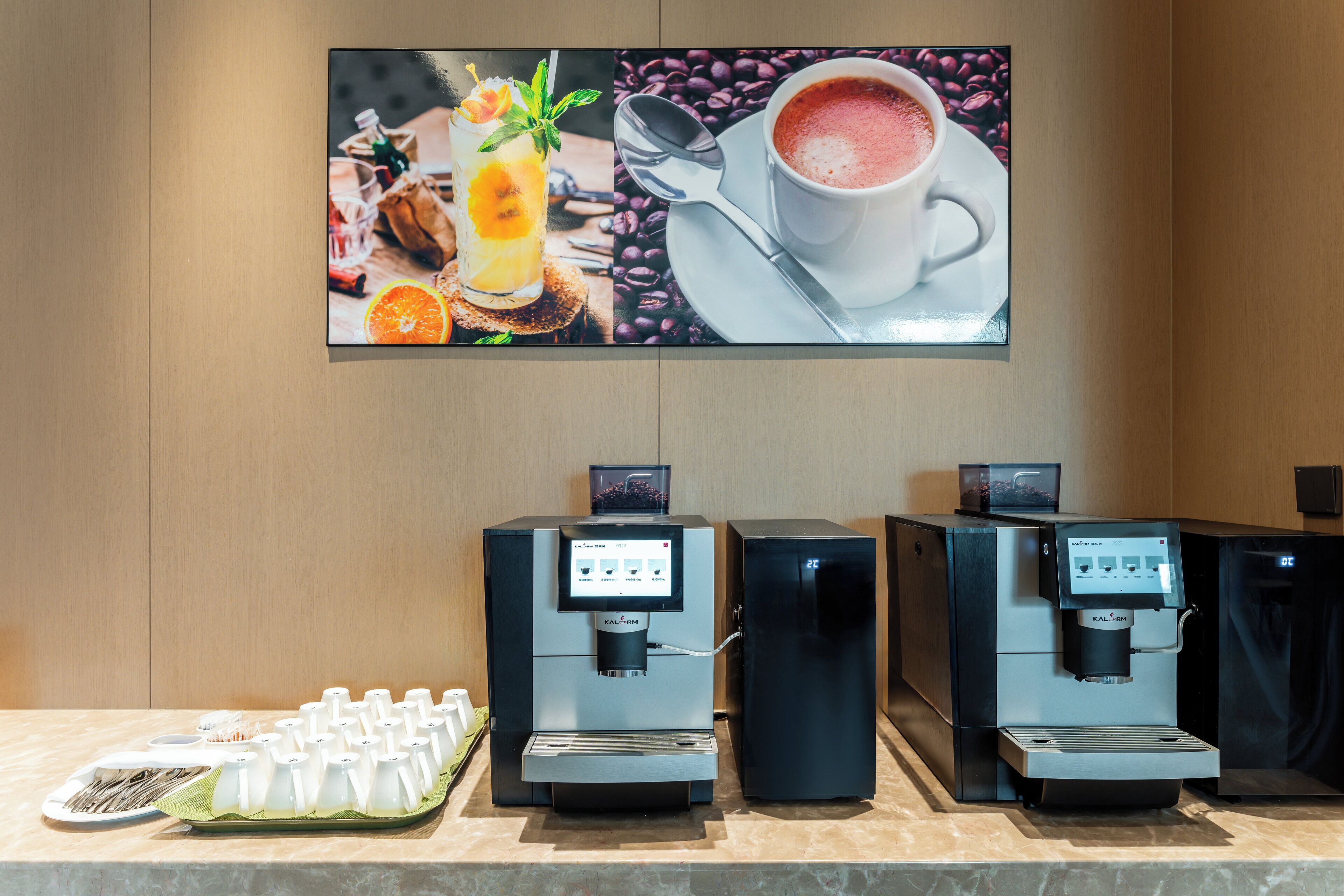A coffee station with multiple espresso machines and a tray of disposable cups.