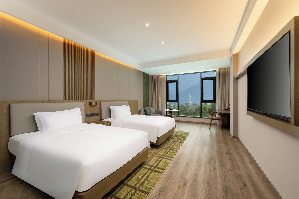 A hotel room with two beds, a desk, and a large window offering a mountain view.
