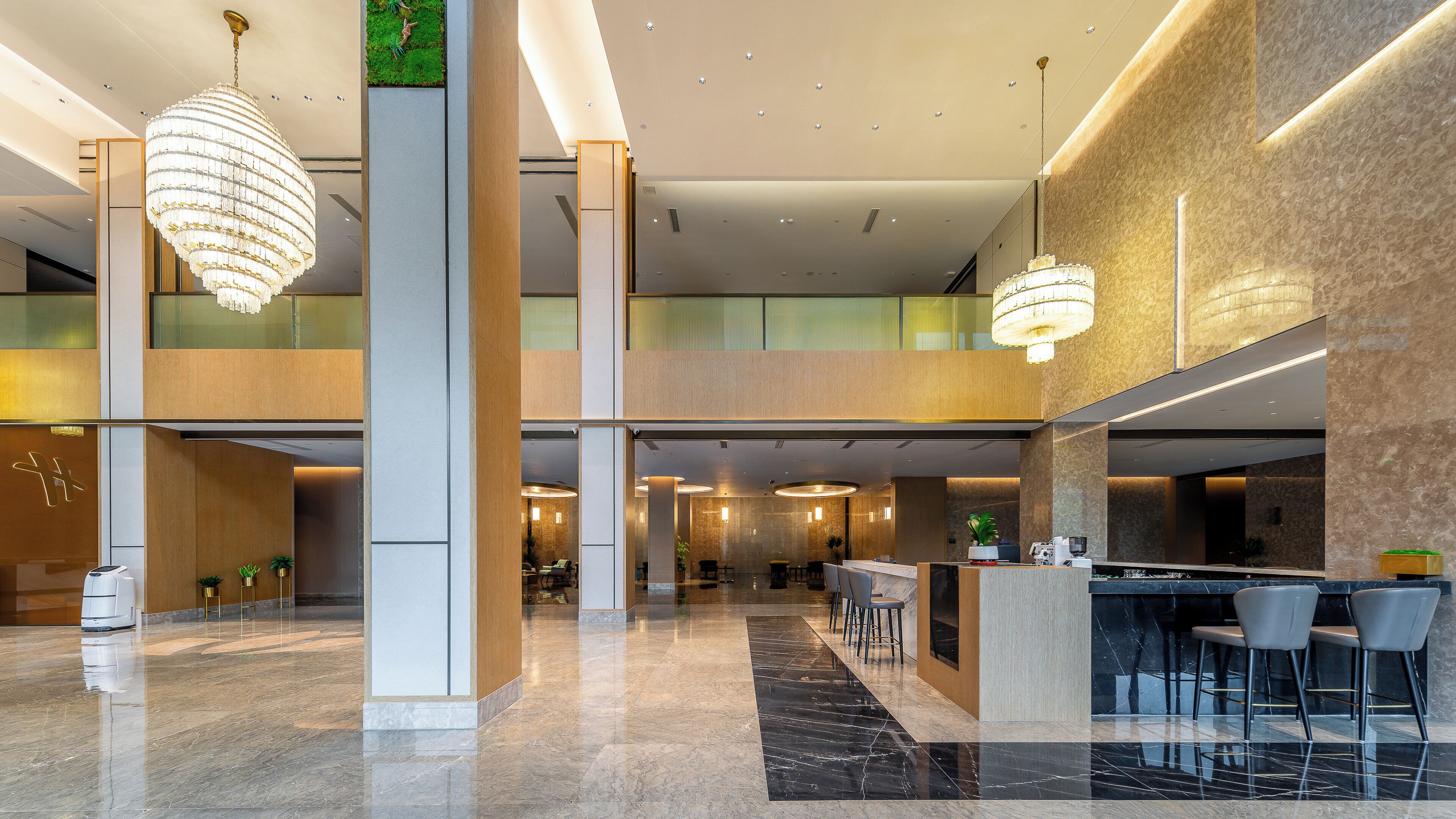 A spacious lobby with a high ceiling, modern chandeliers, a reception desk, and seating areas.