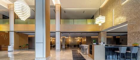 A spacious lobby with a high ceiling, modern chandeliers, a reception desk, and seating areas.