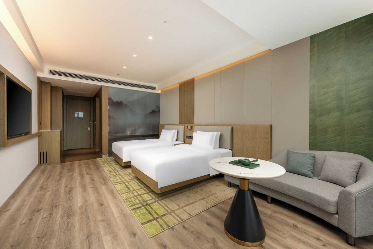 Una habitación de hotel moderna con dos camas, un sofá, una mesita y un televisor.