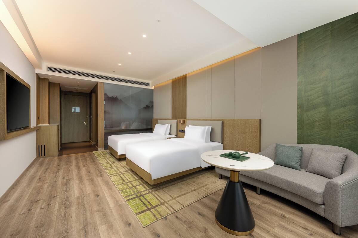 A modern hotel room with two beds, a sofa, a small table, and a TV.