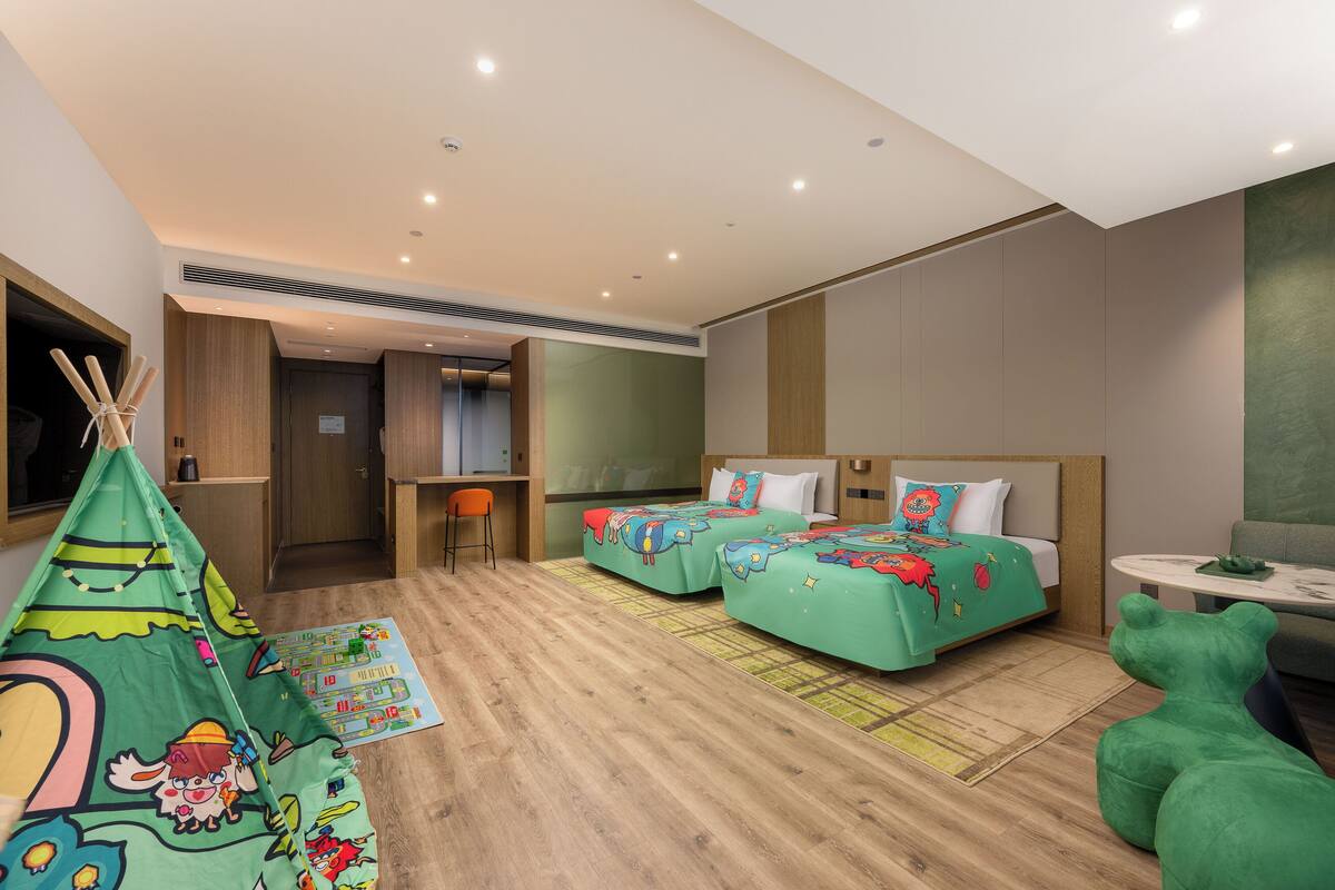 A hotel room with two beds, a desk, a chair, a green sofa, and a tent.
