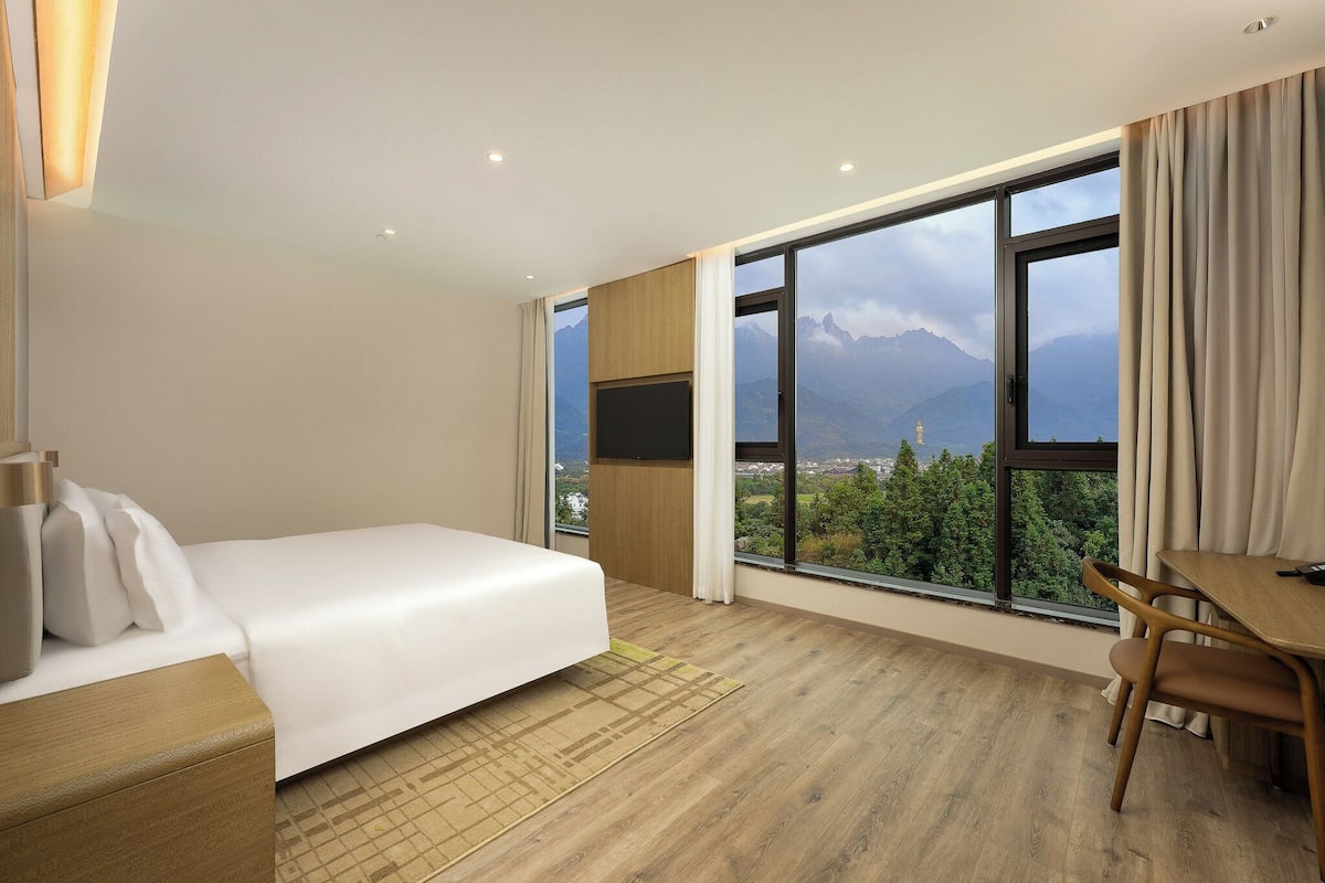 A hotel room with a bed, a desk, and a large window offering a mountain view.