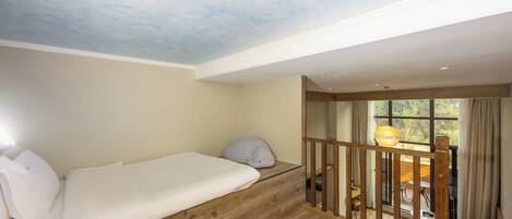 Una habitación con suelo de madera, una cama blanca, un techo con diseño de nubes y vistas a un espacio exterior con una mesa y sillas.