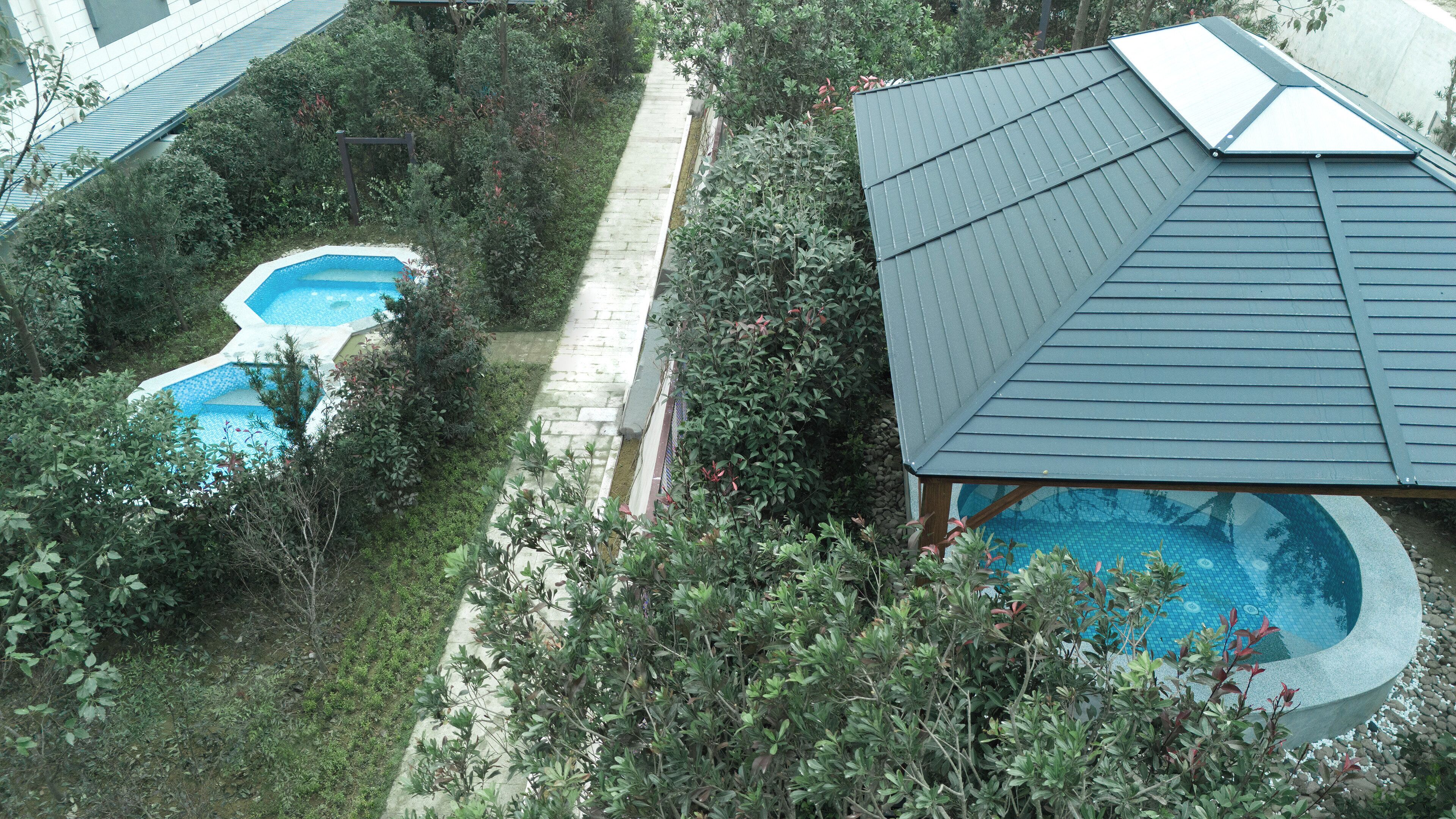 A residential area with a swimming pool, a pathway, and a house with a sloped roof.