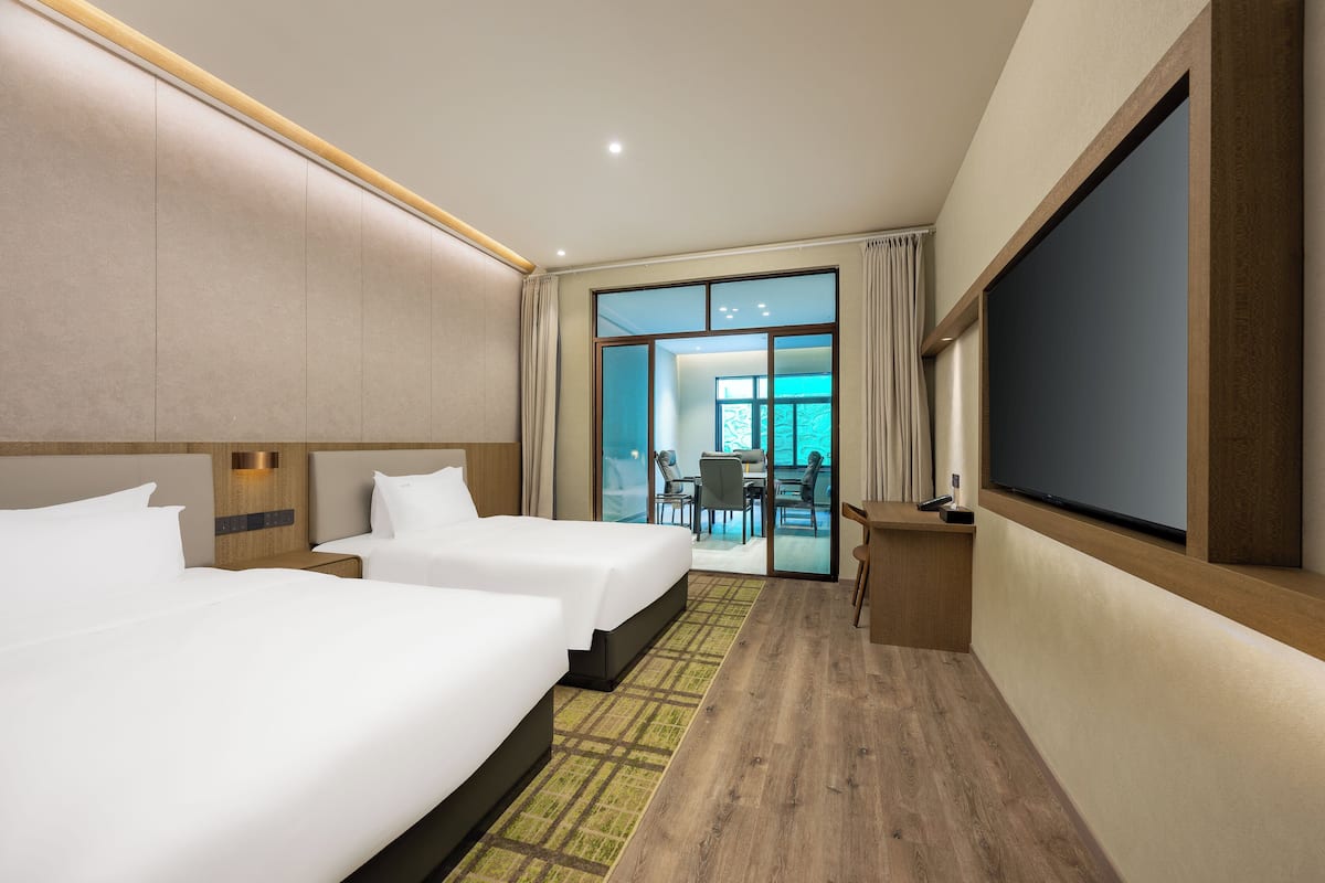 A hotel room with two beds, a flat-screen TV, a desk, and a view of the outside.