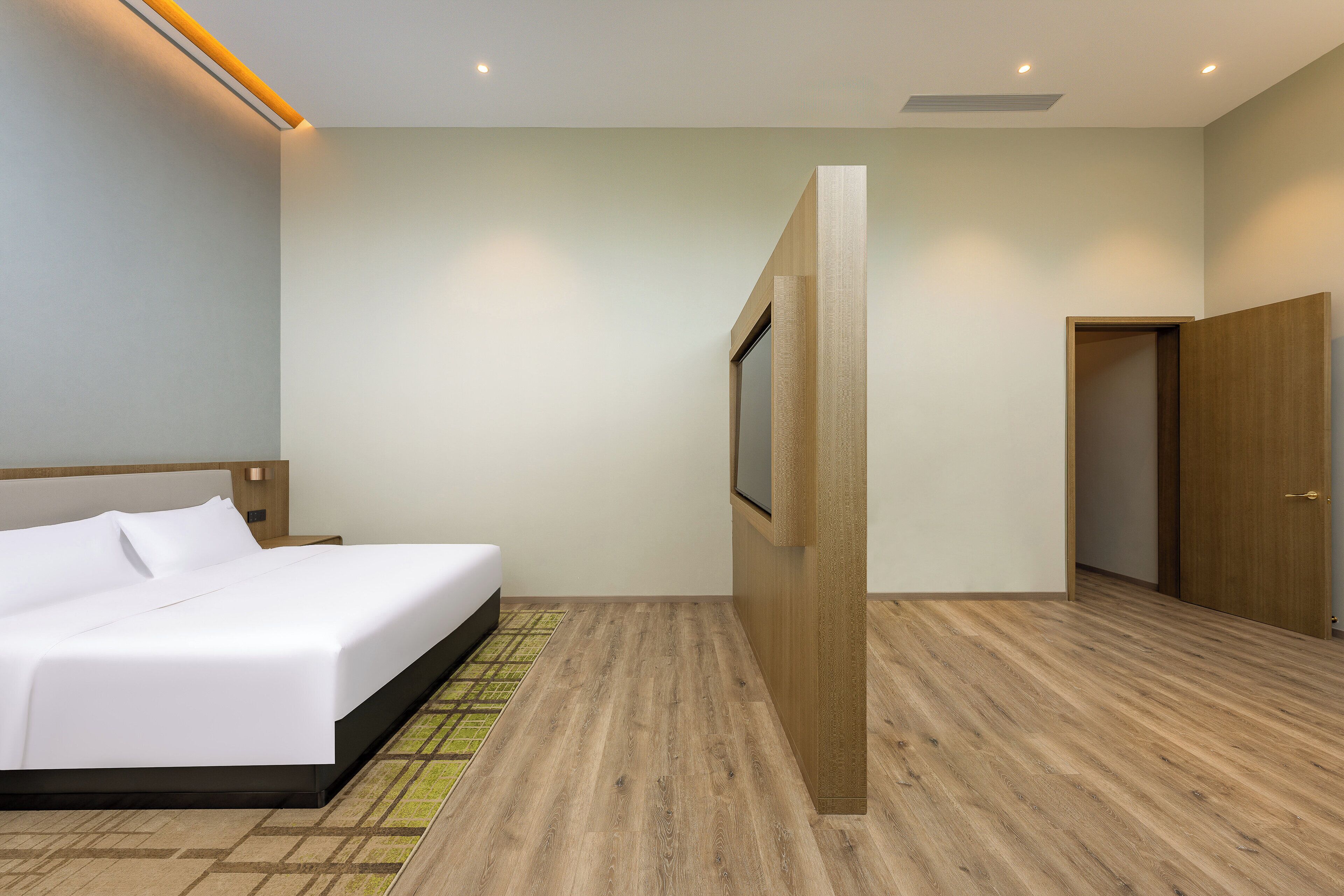 A modern hotel room with a large bed, a wooden floor, a wooden wardrobe, and a door leading to another room.
