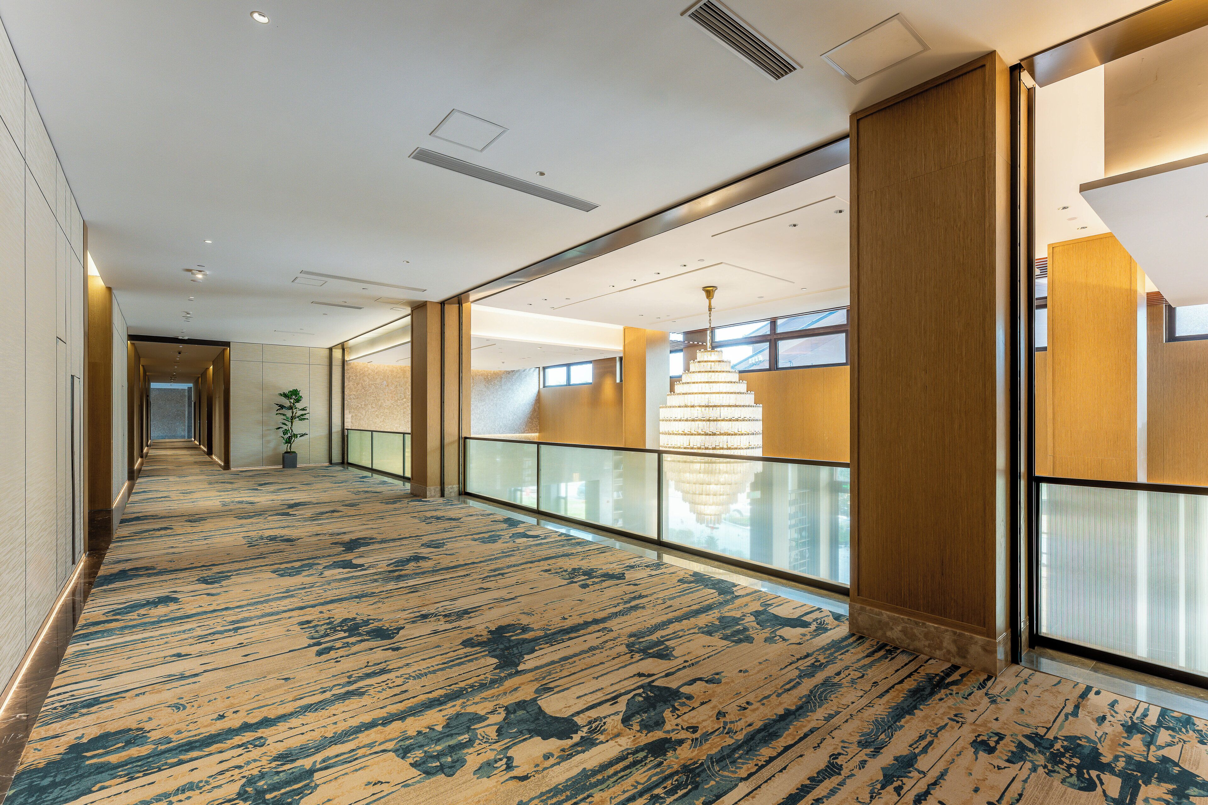 A hotel corridor with a patterned carpet, glass railings, and a chandelier.