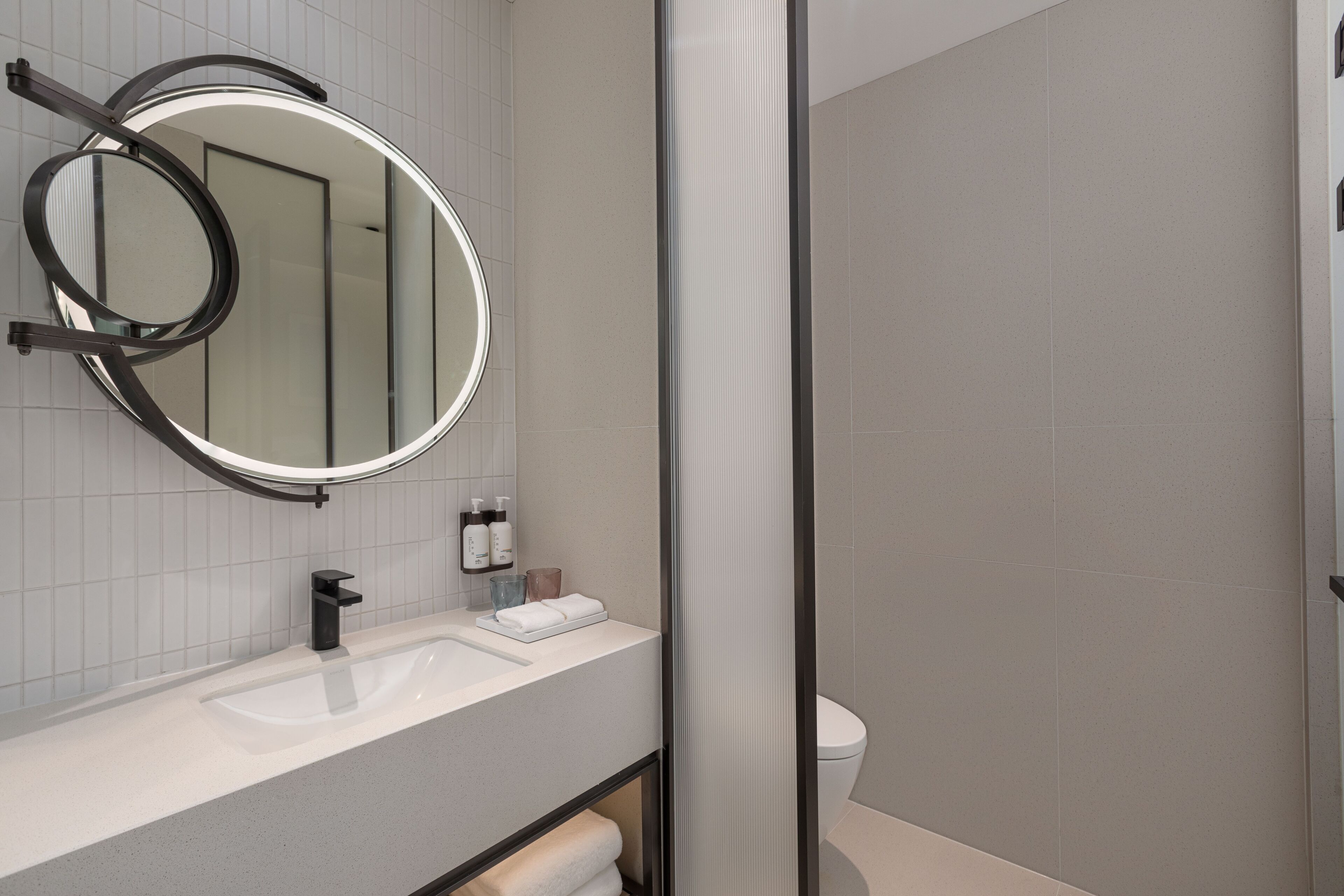 Une salle de bain moderne avec un miroir rond, un lavabo blanc et des toilettes.