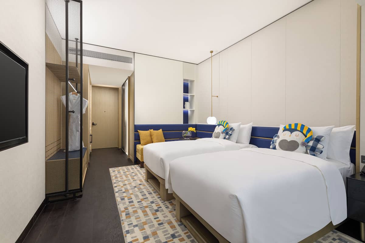 A hotel room with two beds, a large mirror, a wardrobe, and a small table with a lamp.