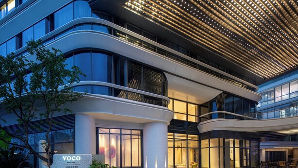 A modern hotel with a curved facade, large windows, and a well-lit entrance area. - voco Suites Shanghai Hongqiao CBD by IHG (Shanghai)