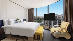 Habitación de hotel moderna con una cama grande, un área de estar, televisión y vistas a la ciudad.