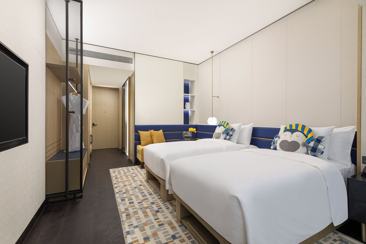 Habitación de hotel con dos camas, un espejo grande, un armario y una mesita de noche con lámpara.