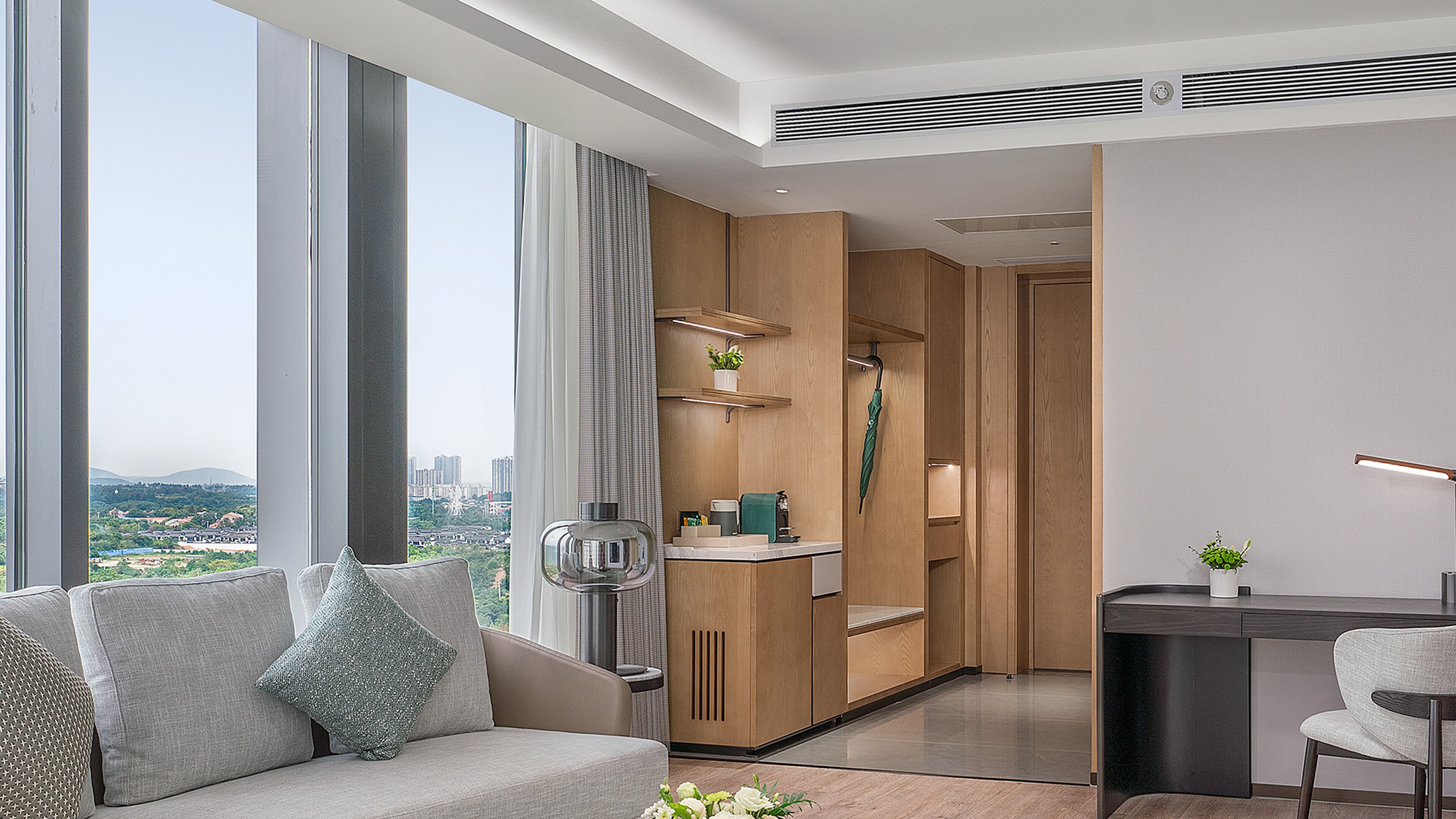 Quarto de hotel moderno com uma janela grande, um sofá, uma escrivaninha e uma cozinha compacta.
