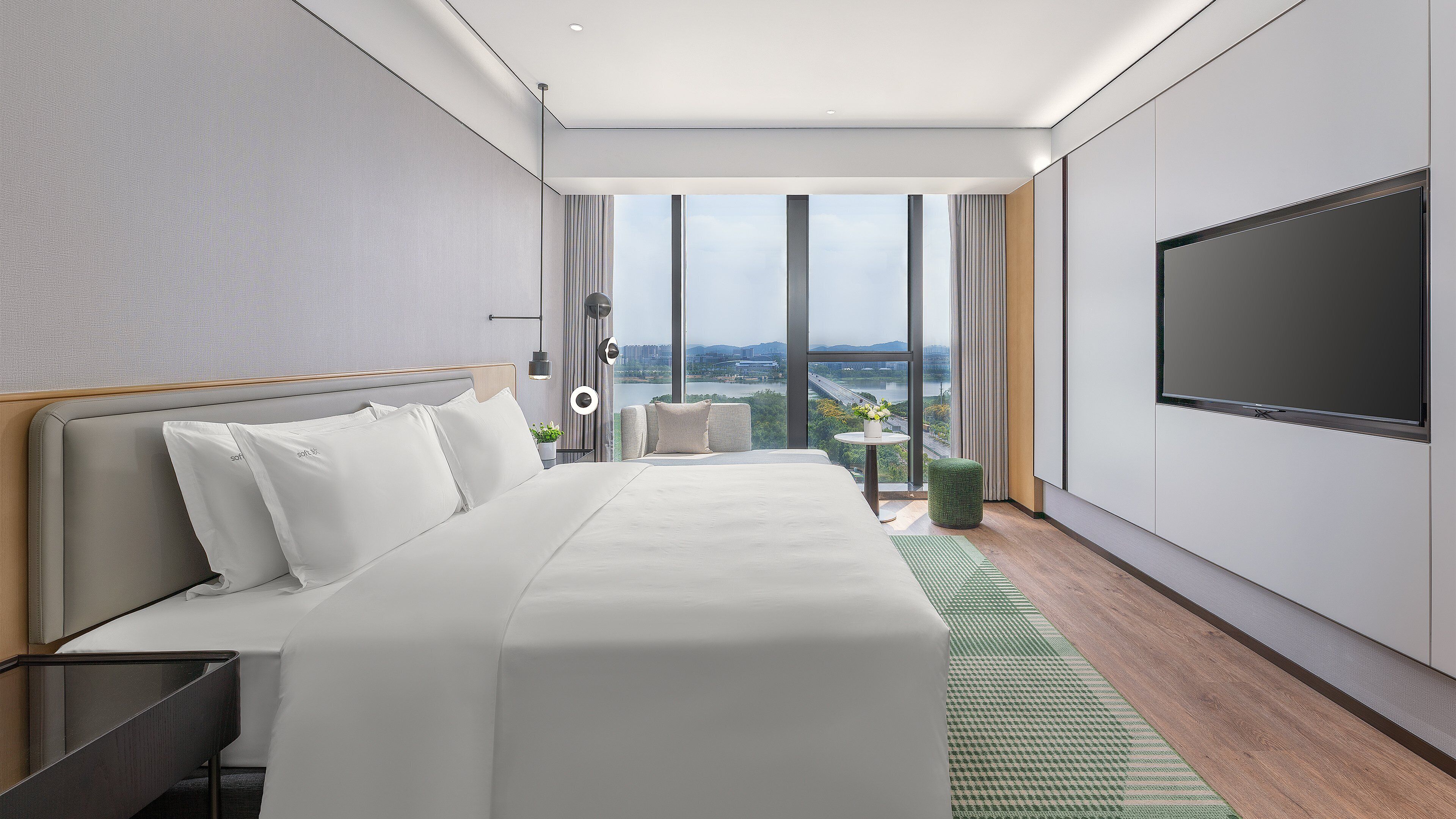 Moderni hotellihuone, jossa on suuri sänky, oleskelualue, televisio ja näkymä kaupunkiin.