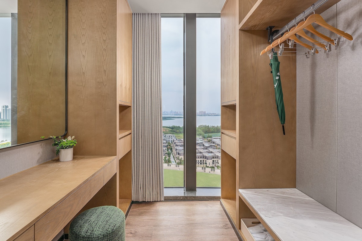 A modern bathroom with a large window, wooden vanity, and a green plant.