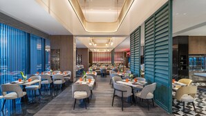 A modern restaurant with a central seating area, a bar, and a view of the cityscape through large windows. - Holiday Inn Wuhan Houguan Lake by IHG (Wuhan)