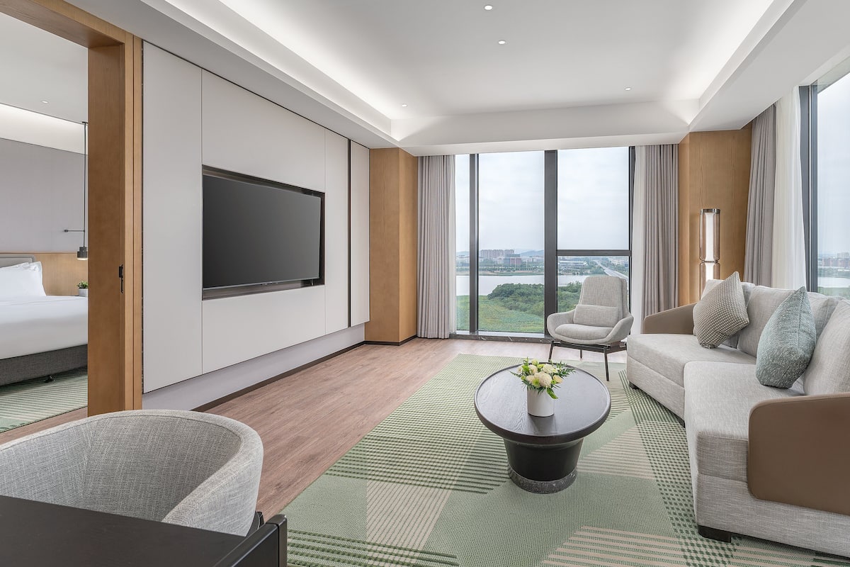 A modern hotel room with a large bed, a sofa, a coffee table, and a TV.