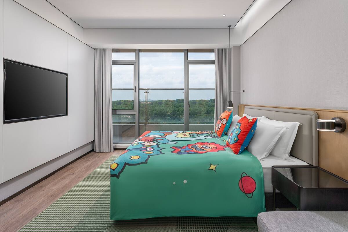 A modern hotel room with a large bed, a flat-screen TV, and a view of the outdoors.