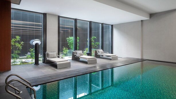 A modern indoor pool area with lounge chairs and a glass-enclosed view of a garden. - Holiday Inn Wuhan Houguan Lake by IHG (Wuhan)