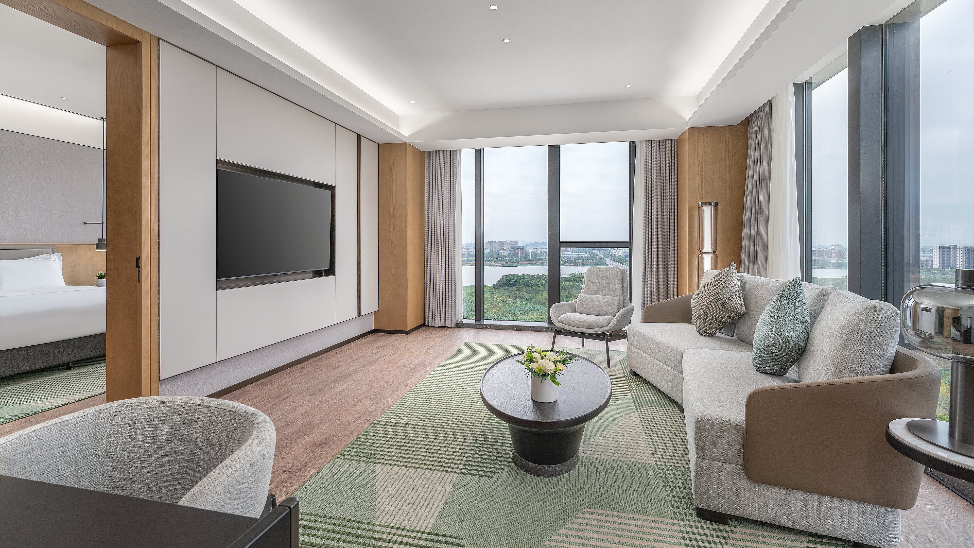 A modern hotel room with a large bed, a sofa, a coffee table, and a TV.
