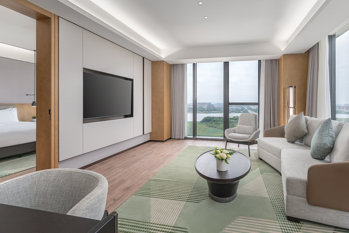 A modern hotel room with a large bed, a sofa, a coffee table, and a TV.
