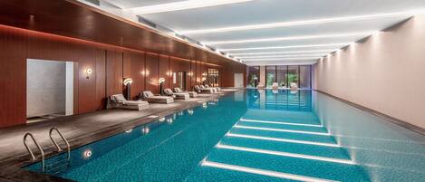 A long indoor swimming pool with multiple lounge chairs and a clear view of the pool's edge.