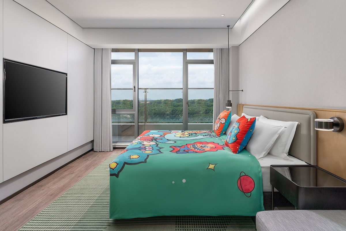 A modern hotel room with a large bed, a flat-screen TV, and a view of the outdoors.