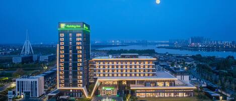 Un hotel Holiday Inn con una torre destacada, un edificio grande de varios pisos y un área de estacionamiento bien iluminada.