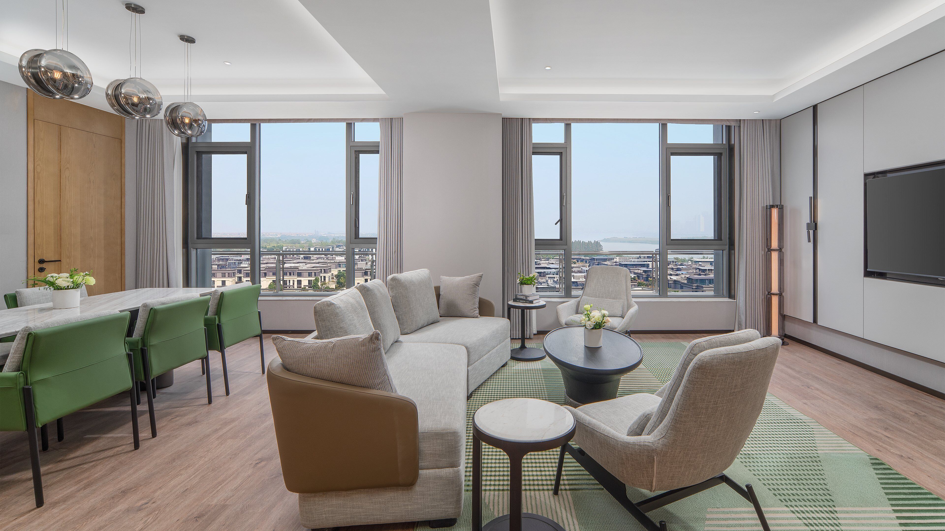 Un salon moderne comprenant un canapé, des fauteuils, une table à manger et un téléviseur. De grandes fenêtres offrent une vue sur la ville.