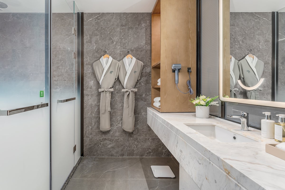 A modern bathroom with a glass shower enclosure, a wooden vanity, and two robes hanging on hooks.