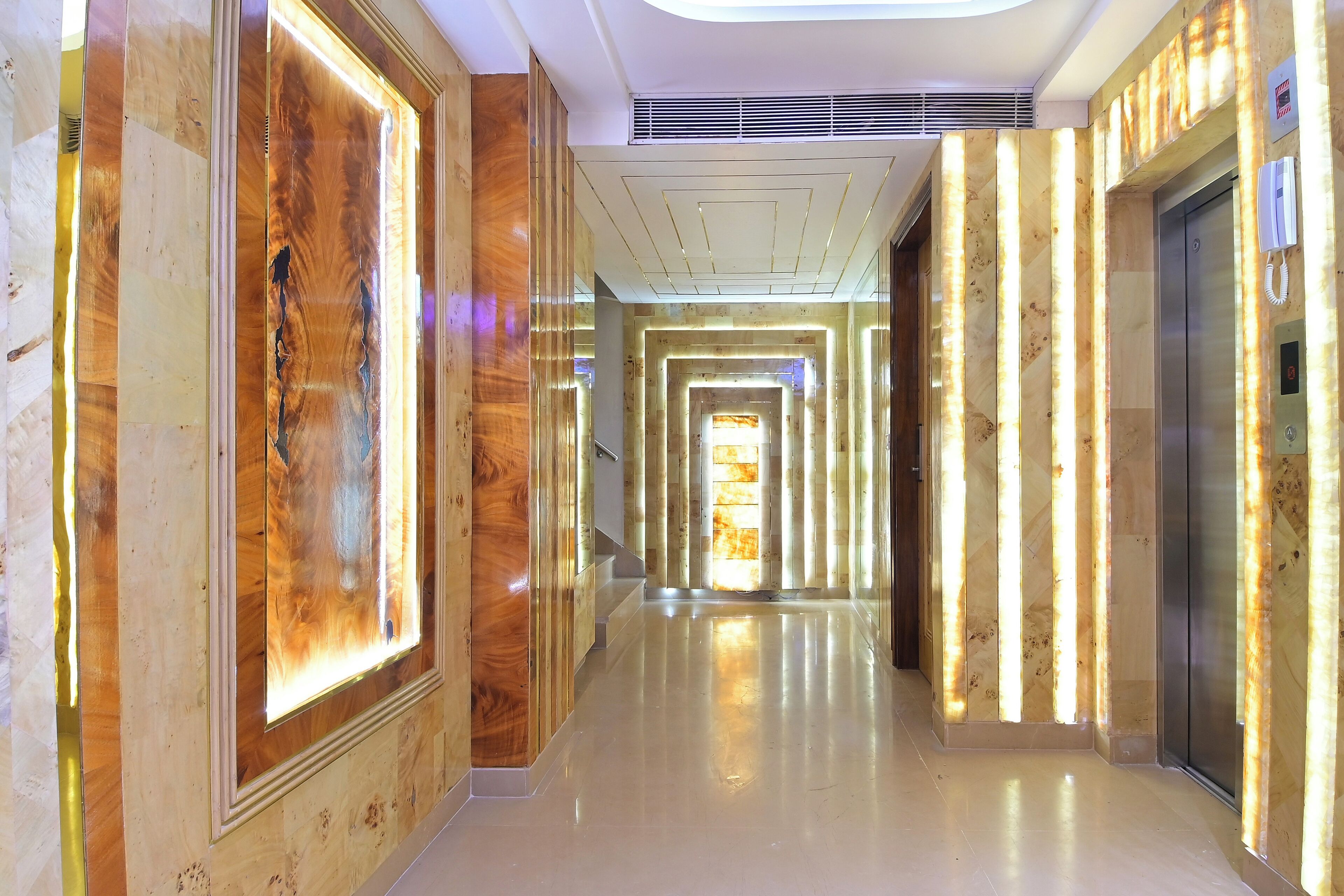 A modern hotel corridor with a polished floor, wooden paneling, and an elevator.