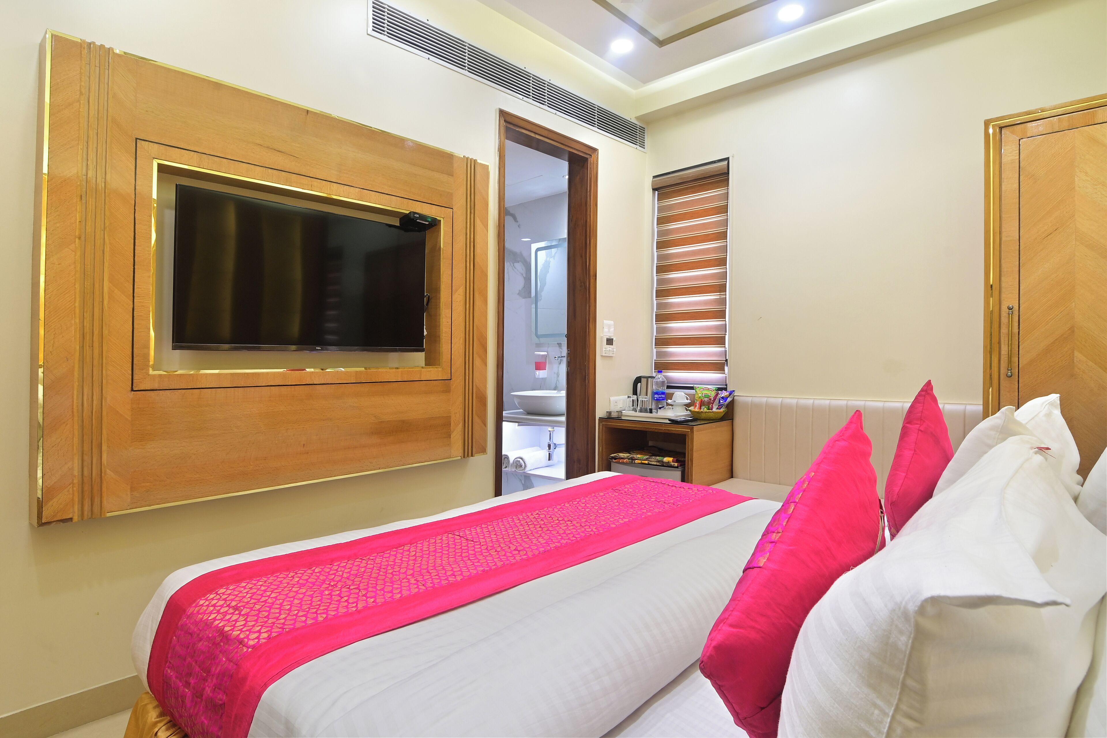 A hotel room with a bed, a TV mounted on the wall, a wooden door, and a radiator.